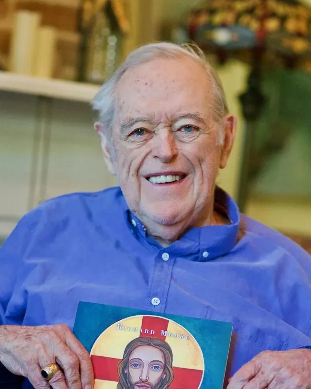 Richard Moore, smiling, holding his book.